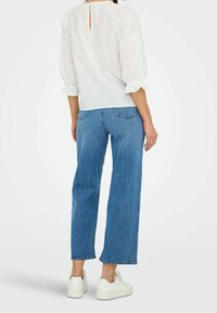 Weiße Bluse mit Puffärmeln und einer Schlüsselloch-Details am Rücken, kombiniert mit hochtaillierten, geraden blauen Jeans und weißen Turnschuhen.