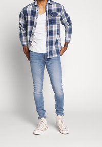 Rutig flanellskjorta i blått över en vit t-shirt, matchad med ljusblå skinny jeans och vita högklackade sneakers.