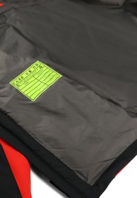 Giacca nera e rosso brillante con una superficie liscia e lucida. Presenta un grande etichetta verde neon con un layout a griglia per il tracciamento delle informazioni.