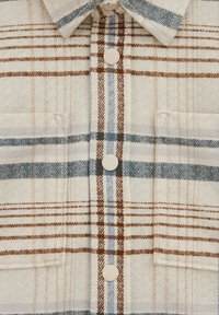 Skjorta med knappar i beige med rutmönster i blått, brunt och ljust tan. Har en spetsig krage och två bröstfickor. Mjuk textur.