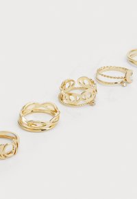 Conjunto de cinco anillos de oro con diversos diseños: retorcidos, con formas recortadas, acentos trenzados y un solo gema en uno de los anillos.