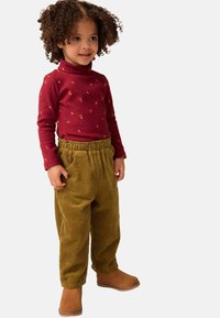 Un pull à col roulé rouge à manches longues avec de petits motifs jaunes, associé à un pantalon en velours côtelé jaune. Bottes cheville brunes, tissu texturé, coupe décontractée.
