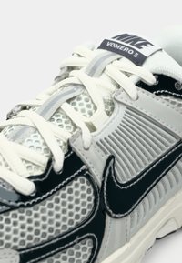 Die Nike Vomero 5 Sneakers in Hellgrau mit schwarzen Akzenten verfügen über ein Obermaterial aus Mesh, strukturierte Einsätze und weiße Schnürsenkel, die die Belüftungsdetails hervorheben.