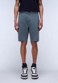 Shorts de carga grises con bolsillos laterales, confeccionados en tejido ligero. Llevados con calcetines oscuros hasta la rodilla y zapatillas deportivas azul marino.