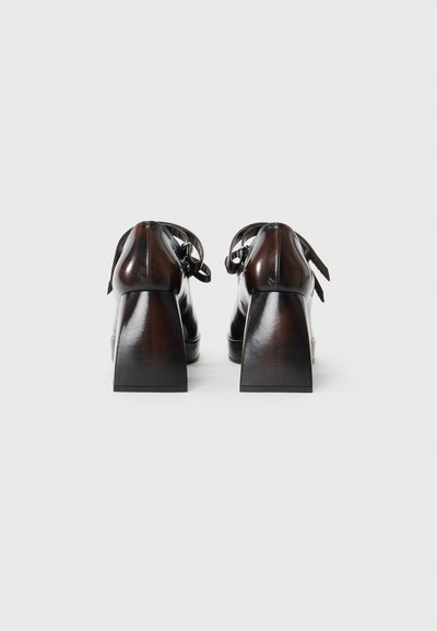Chaussures à talons en cuir marron avec un talon carré, dotées d'un laçage avec des accents de ruban. Texture lisse, design minimaliste.