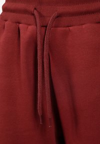 Bordowe dresowe spodnie z ribbowanym elastycznym pasem i dopasowanym sznurkiem. Gładka tekstura i luźny krój z detalami w formie plis.