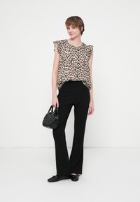 Lagani bluzon s leopard printom s volanima, u kombinaciji s uskim crnim hlačama i malom crnom torbicom, što naglašava ležeran izgled.