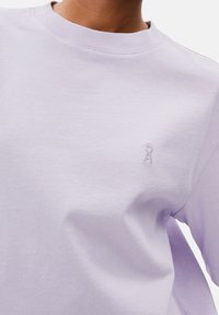 Lilafärgad bomulls-T-shirt med rund hals, korta ärmar och en liten broderad logotyp på vänster bröst. Texturerad tyg, avslappnad passform.