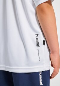 Vit sporttröja med korta ärmar, med en framträdande svart logotyptext på sidan. Slät tygtextur, avslappnad passform.