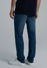 Ciemnoniebieskie dżinsy o prostym kroju, z dwiema kieszeniami z tyłu z haftowanym wzorem, połączone z białymi trampkami.