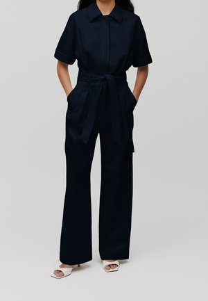 Marineblauer Jumpsuit mit kurzen Ärmeln, Kragen, tailliertem Gürtel und weitem Hosenbein. Mit Seitentaschen und glattem, strukturiertem Stoff.