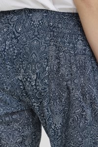 Nærbillede af marineblå bukser med elastisk taljebånd, dekoreret med et hvidt, indviklet mønster af blomster og prikker, båret med en hvid skjorte stukket ind.