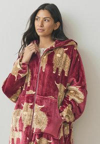Red plush hoodie with beige Highland cow pattern. Features a front zipper and pockets, made of soft, textured fabric.