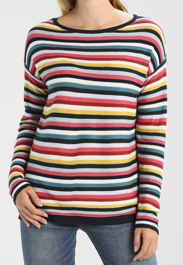 Femme portant un pull à manches longues à rayures horizontales rouges, jaunes, bleues, blanches et noires, associé à un jean bleu.