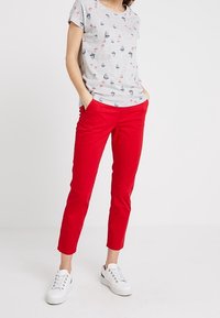 T-shirt en coton gris avec petits motifs imprimés, associé à un pantalon rouge fuselé. Des baskets blanches complètent la tenue. Design simple et coupe décontractée.