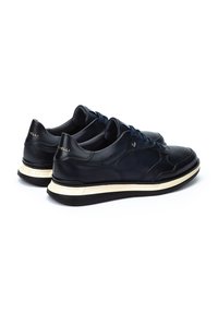 Muške tenisice od crne kože s plavim vezicama, s bež potplatom i suptilnim brendingom na peti, prikazujući glatku teksturu i usklađen dizajn.