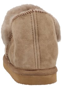 Botte en daim beige avec une doublure en laine moelleuse au niveau du col, présentant des coutures visibles et une semelle en caoutchouc plate. Design simple et arrondi.
