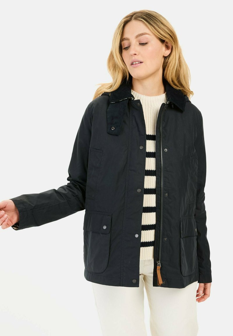 Sort, let jakke med en kordfløjlskrave, trykknapper, to forlommer og lynlås, båret over en stribet sweater.