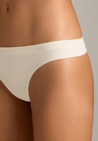 Nærbillede af en persons maveområde iført off-white sømløst undertøj med en ribbet linning mod en neutral baggrund.