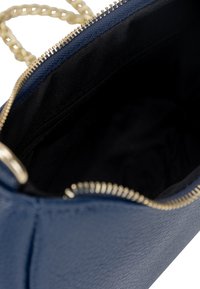 Borsa a mano blu navy con zip dorata e tracolla a catena. L'interno presenta una fodera nera liscia con una tasca con zip per una maggiore sicurezza.