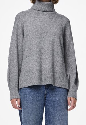 Femme portant un pull gris à col roulé ample avec un ourlet côtelé et un jean bleu taille haute, montrée du cou jusqu'aux hanches.
