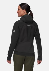 Schwarze Kapuzenjacke mit strukturiertem Rücken und Logodetail. Entworfen mit taillierter Silhouette und Daumenlöchern. Kombiniert mit olivgrünen Hosen.