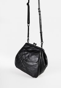 Borsa a tracolla in pelle nera con una forma strutturata, fondo arrotondato, chiusura a patta e tracolla removibile. Presenta una superficie liscia e dettagli di cucitura.