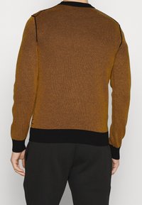 Sweter dziany z fakturowanym wzorem w kolorze musztardowym, czarne ściągacze na mankietach i dole, o swobodnym kroju i okrągłym dekolcie.