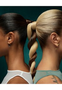 Två frisyrer visas sida vid sida: den ena har slät mörk hår, den andra har en flätad hästsvans med blonda och bruna slingor. Båda bär minimalistiska örhängen.