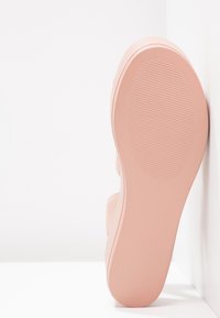 Chaussure rose avec une tige texturée et flexible, conçue pour le confort, équipée d'une semelle en caoutchouc lisse avec un dessous à motifs pour l'adhérence.