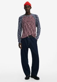 Punane ja sinine muster, pika varrukaga särk ümmarguse kaelusega, koos lahtiste tumedate teksapükste ja mustade saapadega. Heledast punasest kudumüts.