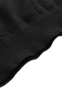 Gros plan sur un tissu noir en maille montrant une texture côtelée et un bord plié sur un fond blanc.