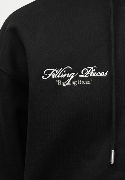 Μαύρο φούτερ με κουκούλα με λευκό κεντημένο κείμενο "Filling Pieces" και μικρότερο κείμενο "Breaking Bread" στο στήθος, με κορδόνι με μεταλλική άκρη.