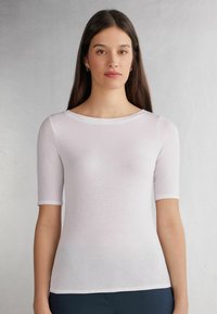 Hvid kortærmet top med rund neckline, lavet af letvægts, blødt stof. Har en tætsiddende silhuet og glat tekstur.