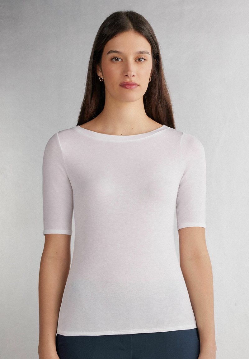 Hvid kortærmet top med rund neckline, lavet af letvægts, blødt stof. Har en tætsiddende silhuet og glat tekstur.