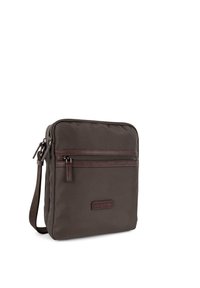 Sac en tissu marron avec une texture lisse, doté d'une poche avant zippée et d'une bandoulière détachable. Accentuée par des garnitures en cuir marron foncé.