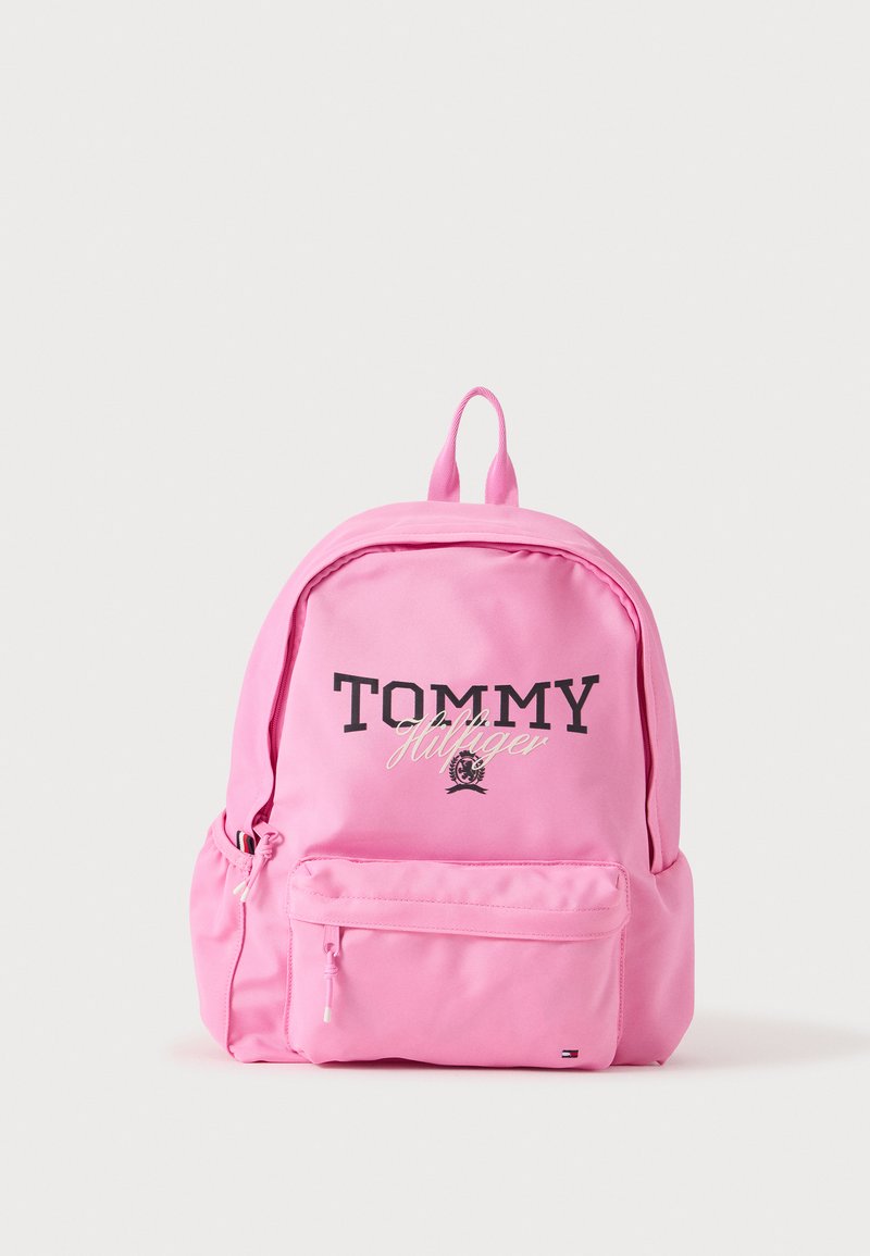 Ροζ σακίδιο πλάτης Tommy Hilfiger με μπροστινή τσέπη με φερμουάρ και λογότυπο της μάρκας σε μαύρο και άσπρο σε απλό ανοιχτό φόντο.