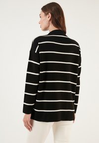 Pulover în dungi alb-negru, cu mâneci lungi, croială relaxată și textură netedă, având dungi orizontale proeminente.