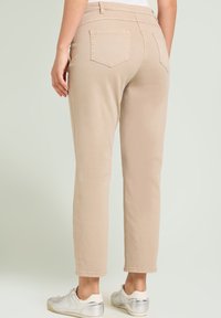 Pantalones de algodón beige con un ajuste cónico, que cuentan con dos bolsillos traseros y una textura suave. Combinados con zapatillas plateadas.