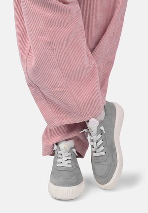 Rosa Cordhosen getragen mit grauen Wildleder-Sneakers mit weißen Sohlen und Schnürsenkeln auf weißem Hintergrund.