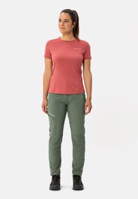Lichtgewicht, kortslippige, rozenkleurige top; groene, taps toelopende broek met naaddetails; gedragen met donkere buitenschoenen.