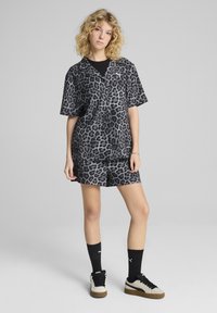 Completo con stampa leopardata in nero e grigio. Maglietta a maniche corte con colletto abbinata a pantaloni corti. Indossato con calze nere e sneaker in tonalità neutra.