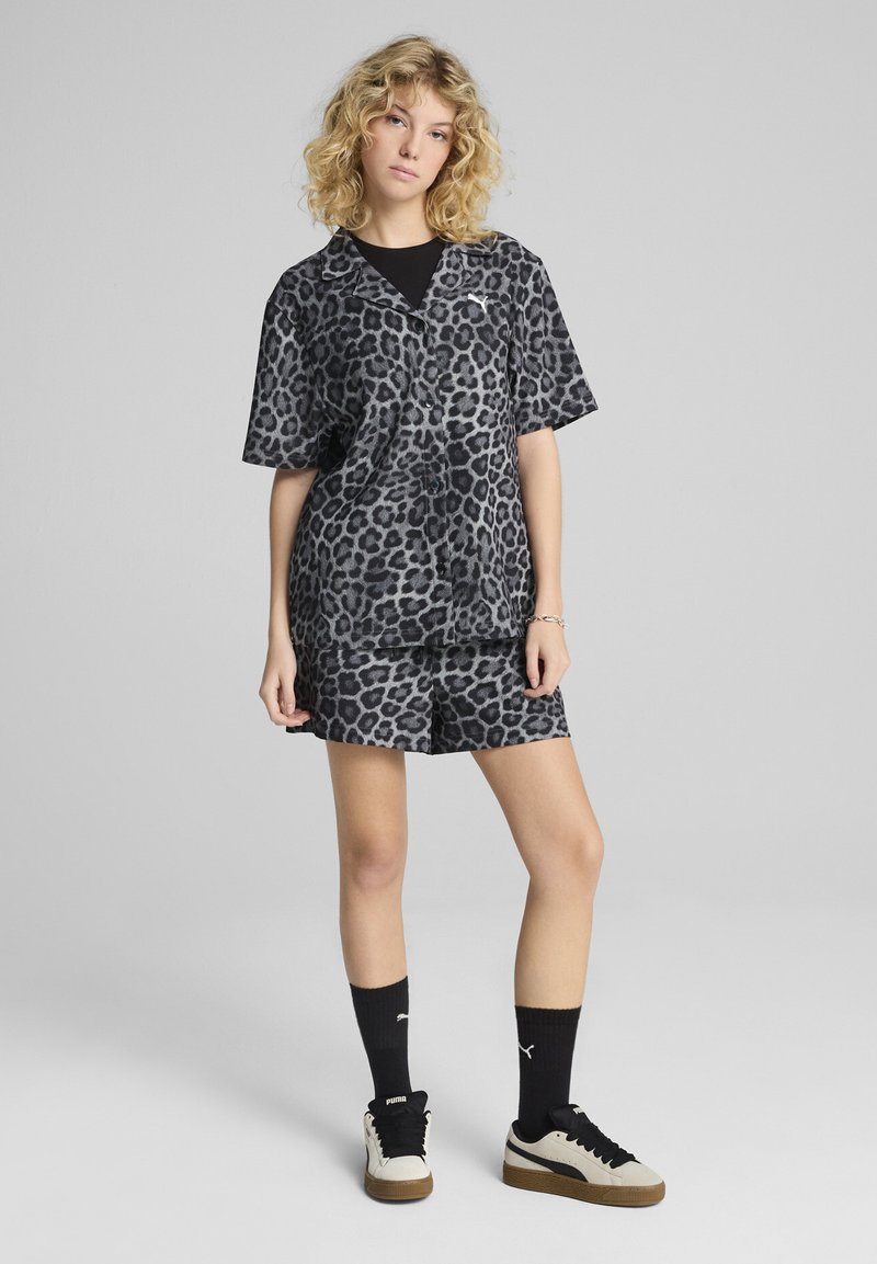 Completo con stampa leopardata in nero e grigio. Maglietta a maniche corte con colletto abbinata a pantaloni corti. Indossato con calze nere e sneaker in tonalità neutra.