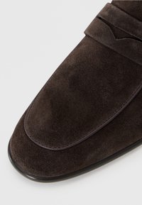 Mocasines de ante marrón con un acabado suave, que presentan un contorno cosido y un sutil detalle dividido en la parte superior, diseño de punta redonda.
