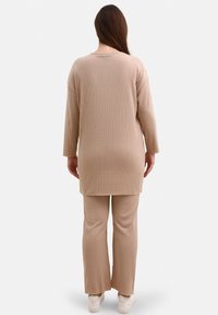 Beige ribbet langærmet top og matchende bukser med en afslappet pasform og tekstur af vandrette striber. Hvide sneakers fuldender outfittet.