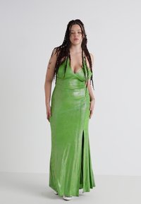 Vestido largo y ajustado de color verde en un material brillante, con escote en V, tirantes finos y una abertura frontal. Textura suave y diseño elegante.