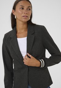 Blazer gris foncé au design structuré, avec une fermeture à un bouton et des accents de poignets rayés. Texture lisse, coupe ajustée.