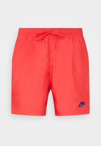 Červené plavecké šortky Nike s elastickým pasem a šňůrkou na stažení, s malým modrým logem Nike na levé noze.