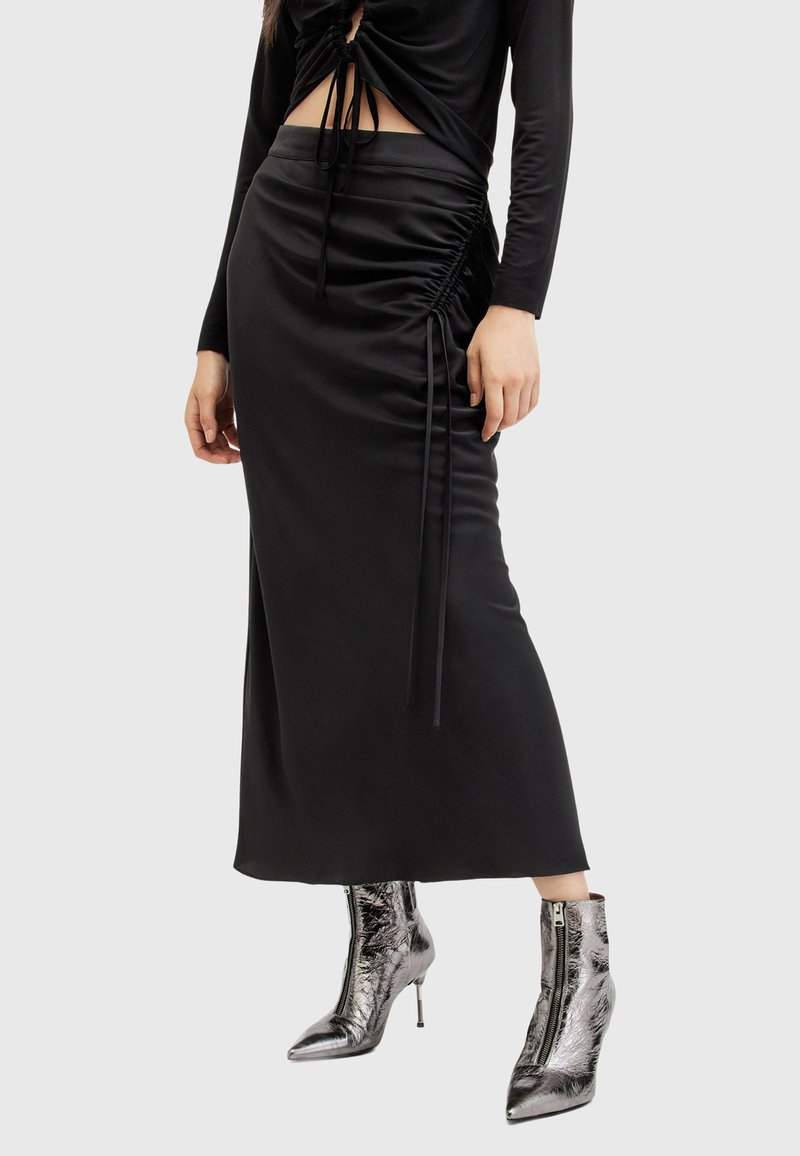 Zwarte satijnen rok met zijsruching, gecombineerd met metallic zilveren enkellaarzen met ritssluiting en een spitse neus.