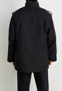 Czarna wodoodporna kurtka z wysokim kołnierzem, naramiennikami i luźnym krojem. Posiada gładką fakturę i długie rękawy.